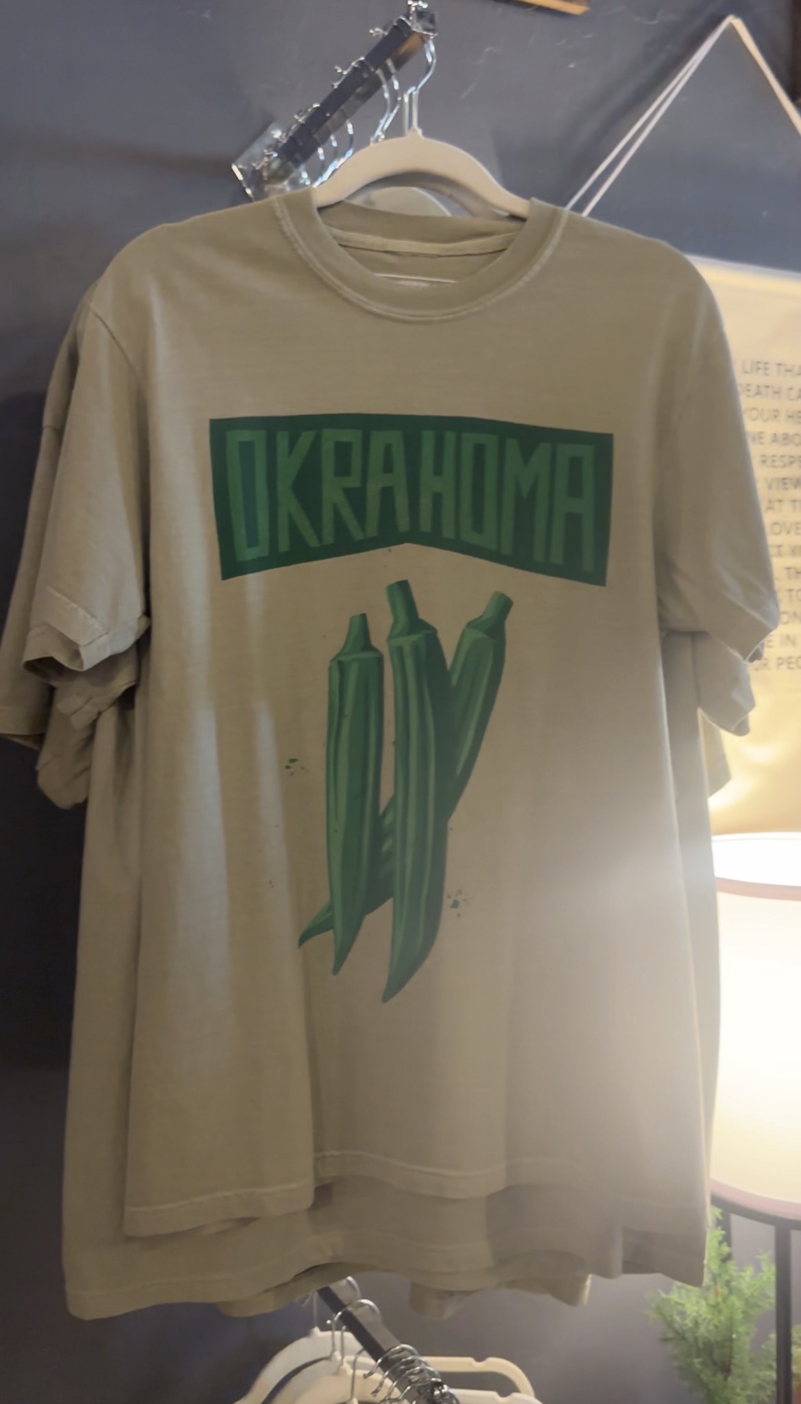 Okrahoma T-shirt with green okra artwork hanging inside Avery Joes Boutique.