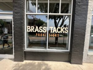 Brass Tacks Provisions storefront window in Midtown OKC with the shop name painted on the glass