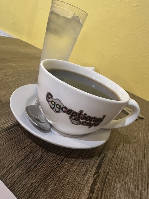 Eggceptional Cafe branded coffee cup on a table with a glass of water.
