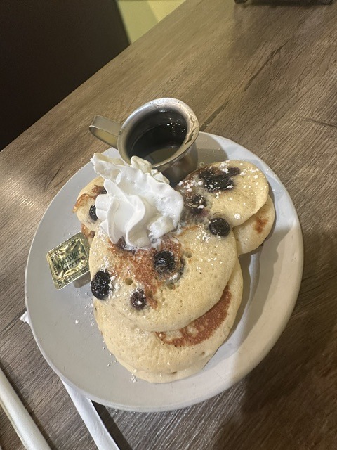 Blueberry pancakes with whipped cream and syrup at Eggceptional Cafe.