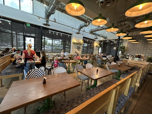 Dining room at Flower Child in Oklahoma City with wooden tables, patterned chairs, and pendant lights.