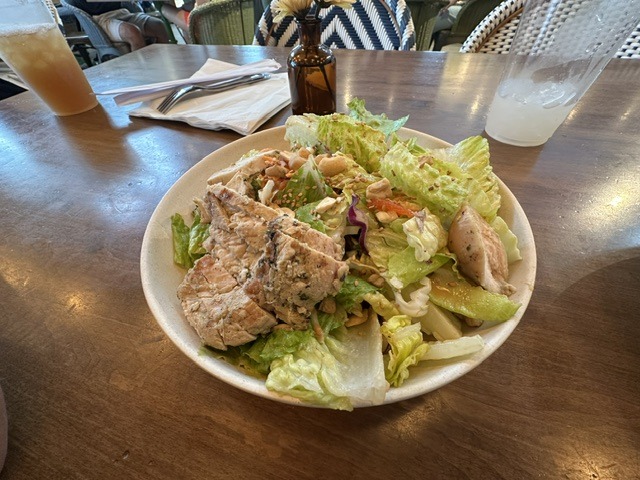 Large salad bowl at Flower Child topped with sliced grilled protein, greens, vegetables, and nuts.