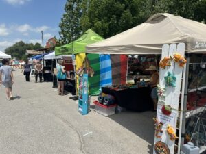 Vendor tents with handmade goods and shoppers at the OKC Farmers Market Summer Solstice Festival.