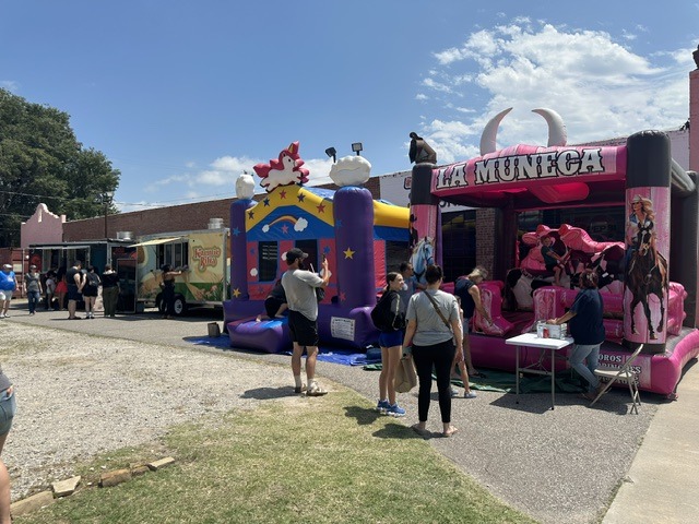Families near colorful bounce houses and a food truck at the OKC Farmers Market Summer Solstice Festival.