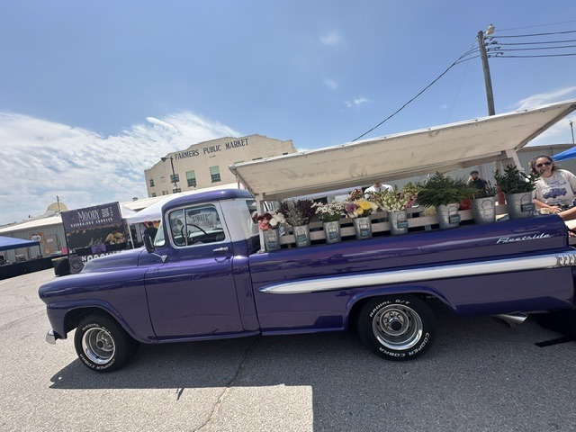 Purple vintage pickup truck filled with flowers in front of the Farmers Public Market building in Oklahoma City.