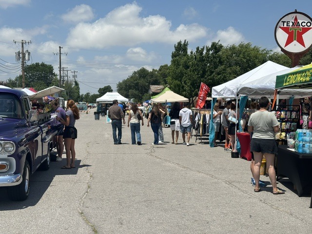 Crowds walking past vendor tents at the OKC Farmers Market Summer Solstice Festival on a sunny day.
