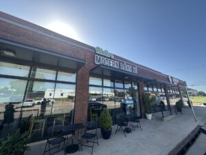 Exterior of Riviere Modern Banh Mi in Oklahoma City with the restaurant sign above the entrance and patio tables out front.