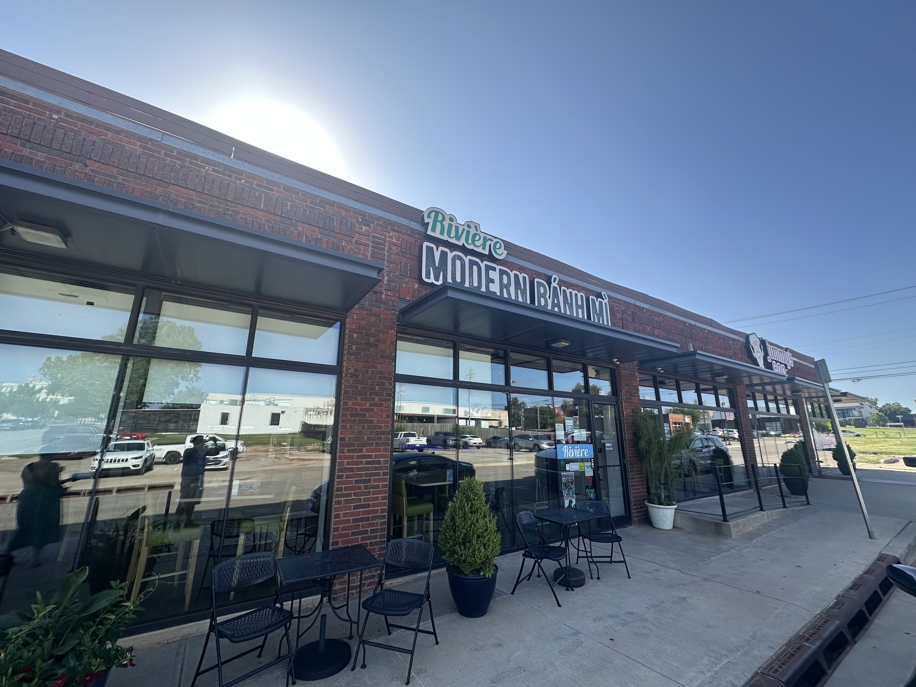 Exterior of Riviere Modern Banh Mi in Oklahoma City with the restaurant sign above the entrance and patio tables out front.