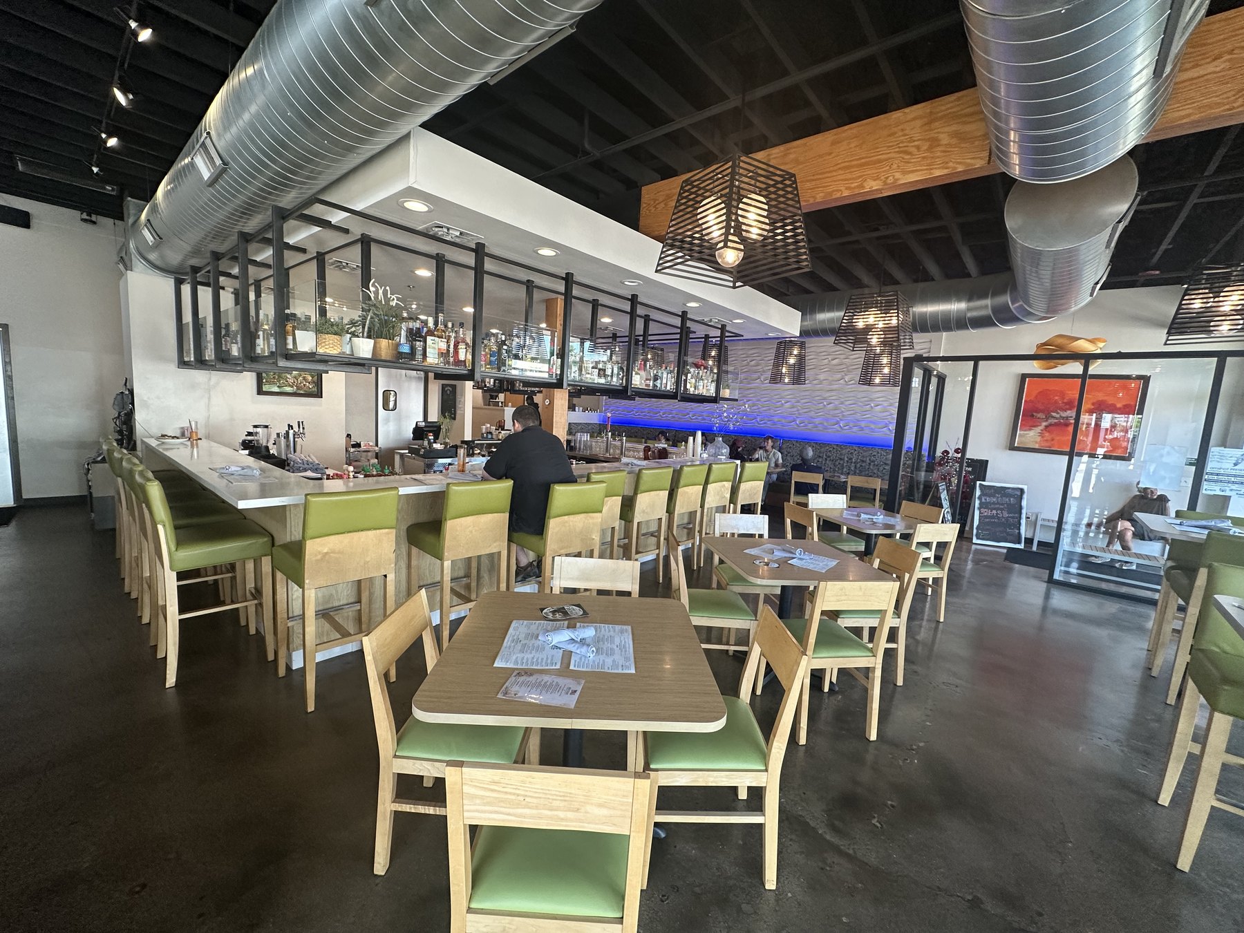 Interior dining room and bar at Riviere Modern Banh Mi in Oklahoma City with tables, green bar stools, and modern lighting.