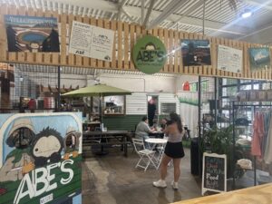 Wide view of ABE’s Campsite inside Sailor & the Dock in Oklahoma City with a camper counter, seating, merch, and customers.