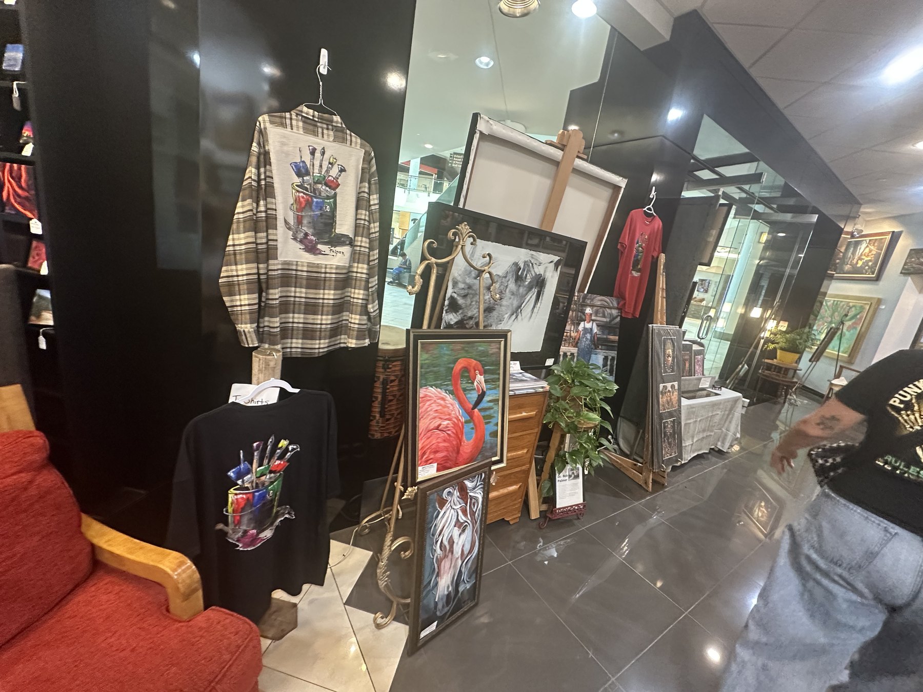 Art Central Gallery display with painted shirts, framed paintings, easels, and artist-made items