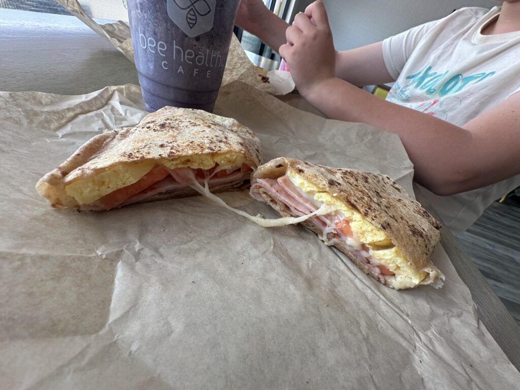 Grilled breakfast sandwich with egg, ham, tomato, and cheese beside a Bee Healthy Cafe smoothie in Edmond, Oklahoma.