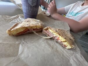Grilled breakfast sandwich with egg, ham, tomato, and cheese beside a Bee Healthy Cafe smoothie in Edmond, Oklahoma.