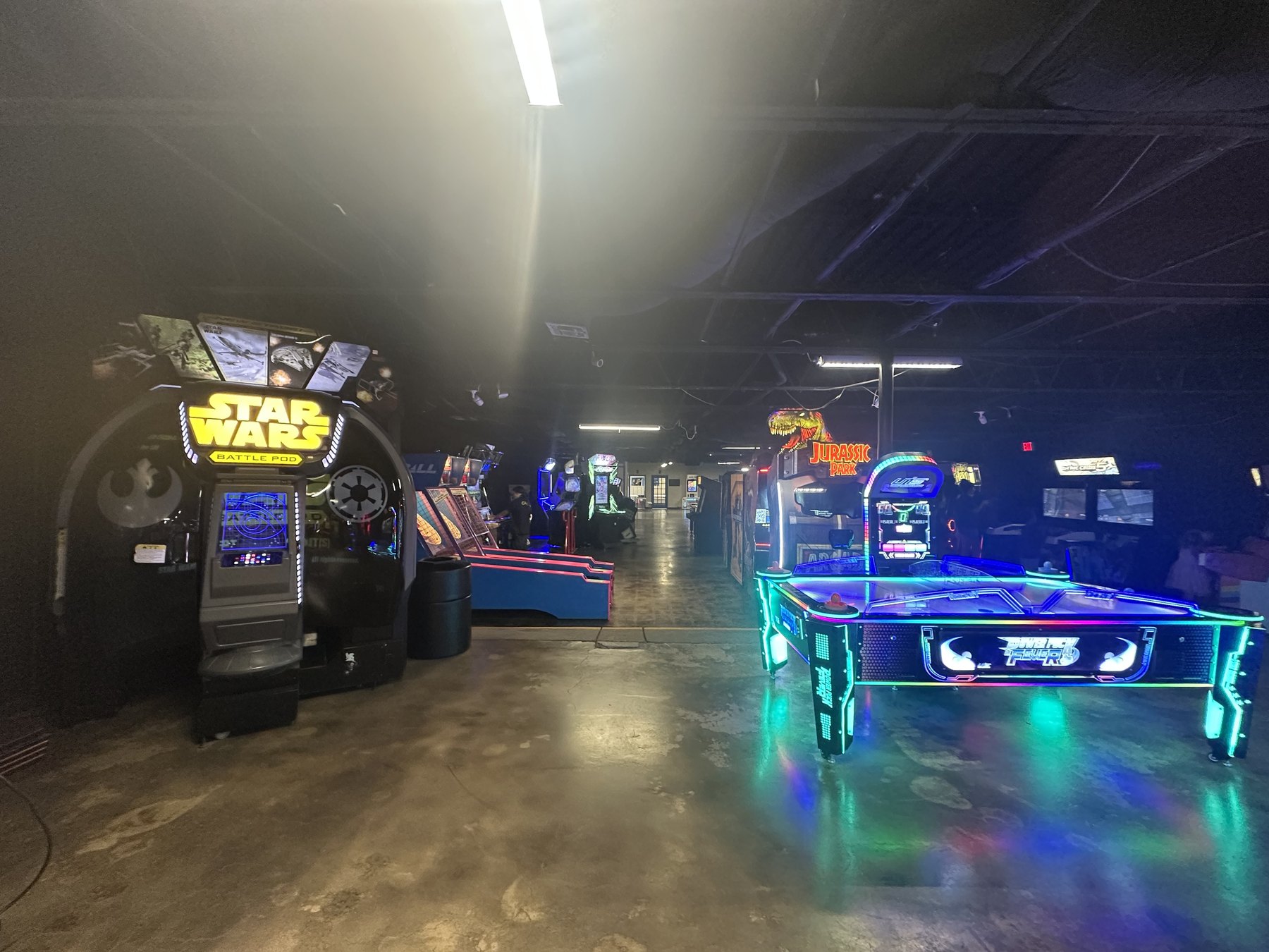 Wide arcade floor at Cactus Jack’s with Star Wars Battle Pod, air hockey, and glowing games.