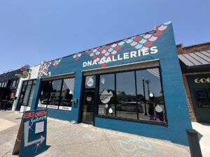 Exterior of DNA Galleries in Oklahoma City's Plaza District with a blue storefront, large windows, and an art show sign on the sidewalk.