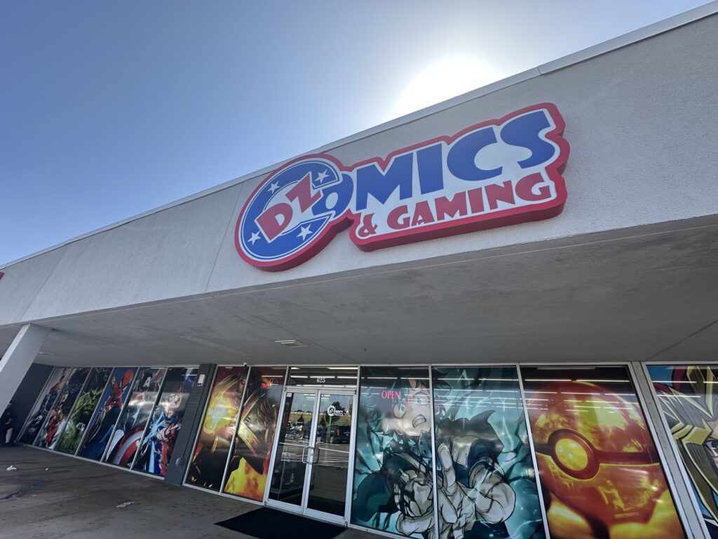 Exterior of DZ Comics & Gaming in Moore, Oklahoma, with a large sign above comic-themed window art.