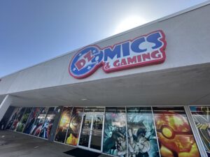 Exterior of DZ Comics & Gaming in Moore, Oklahoma, with a large sign above comic-themed window art.