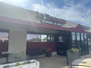 Exterior of La Baguette Bakery and Deli in Oklahoma City with red awning, entrance, patio seating, and storefront sign.