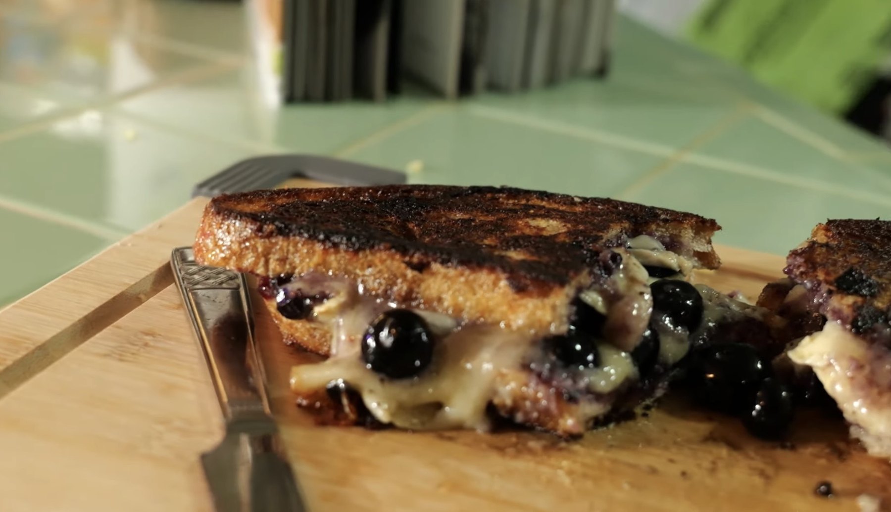 Close-up of a blueberry brie grilled cheese sandwich with melted cheese and blueberries between toasted bread.