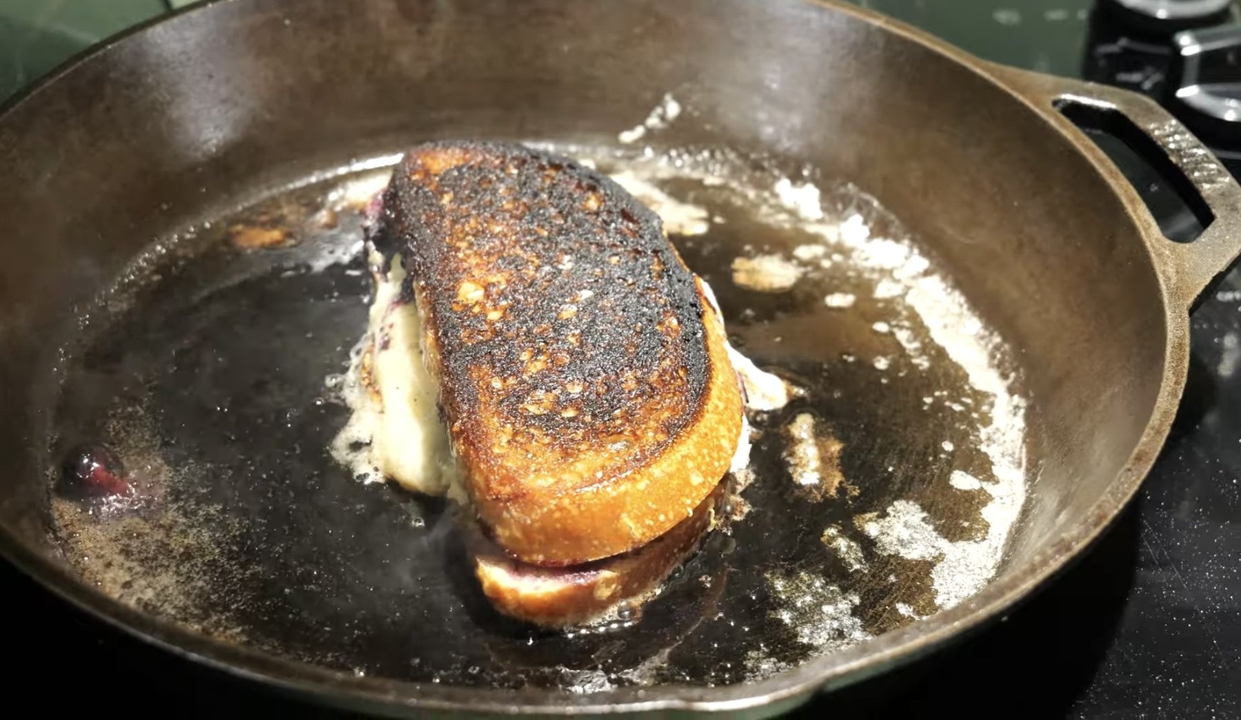 Blueberry brie grilled cheese cooking in a cast-iron skillet with melted cheese and butter around it.