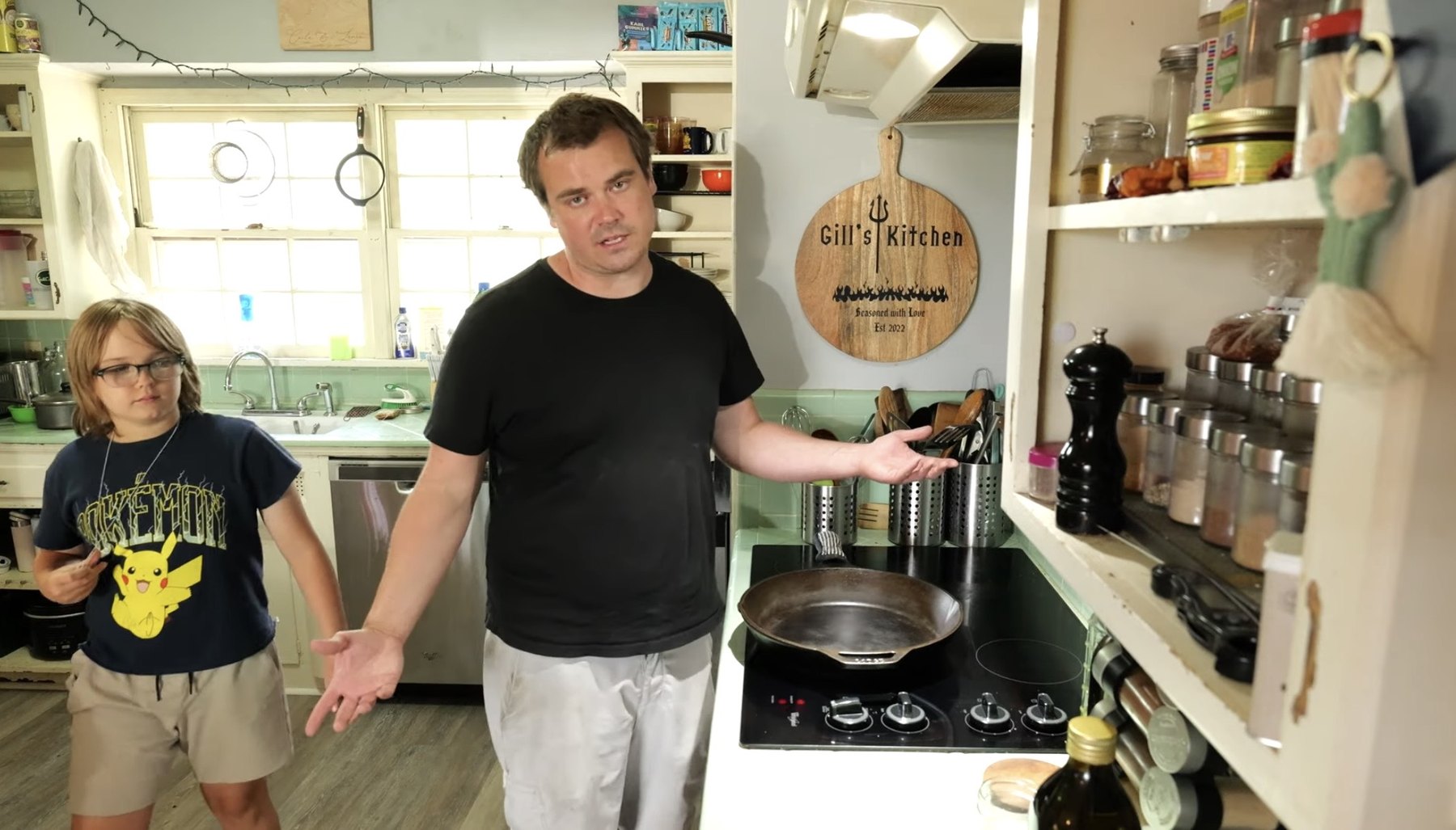 Adult and child stand in a home kitchen beside a stovetop with a cast-iron skillet ready for grilled cheese.