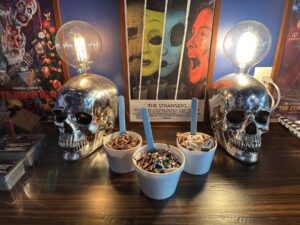 Three ice cream cups at The Ice Creamatory in Norman displayed between chrome skull lamps and horror movie posters.