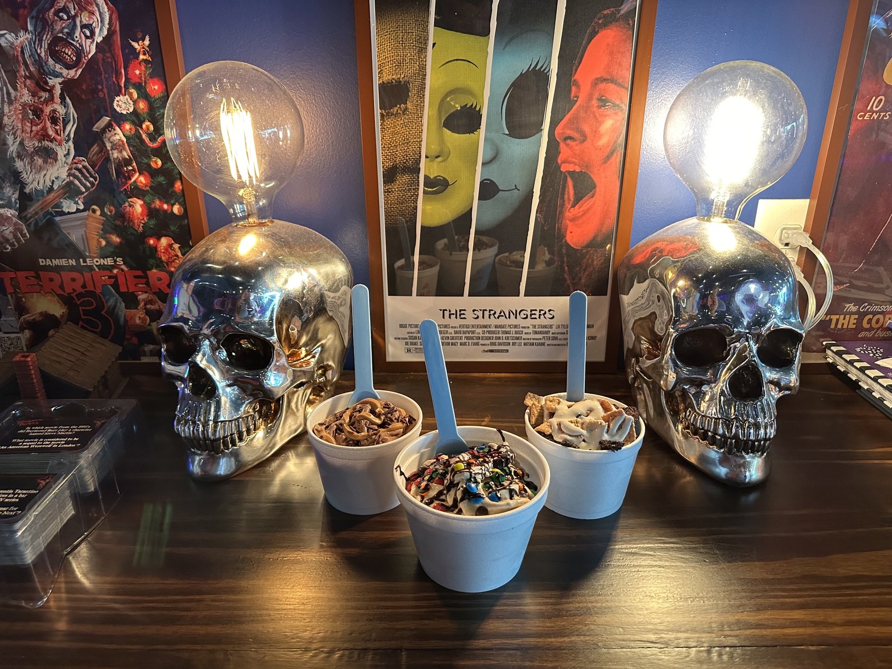 Three ice cream cups at The Ice Creamatory in Norman displayed between chrome skull lamps and horror movie posters.