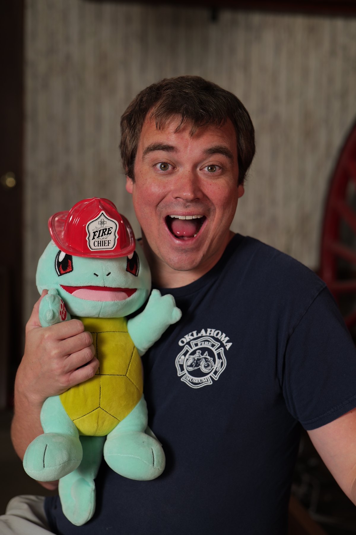 Participant in an Oklahoma Fire Museum shirt smiles while holding a plush toy wearing a Fire Chief helmet.