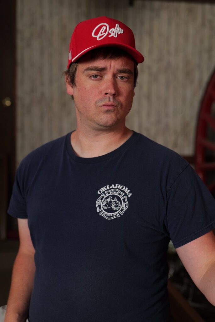 Participant in an Oklahoma Fire Museum shirt wears a red Oklahoma cap during a portrait fundraiser shoot.