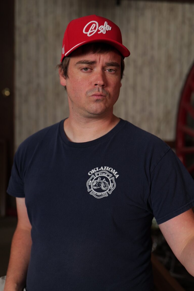 Participant in an Oklahoma Fire Museum shirt wears a red Oklahoma cap during a portrait fundraiser shoot.