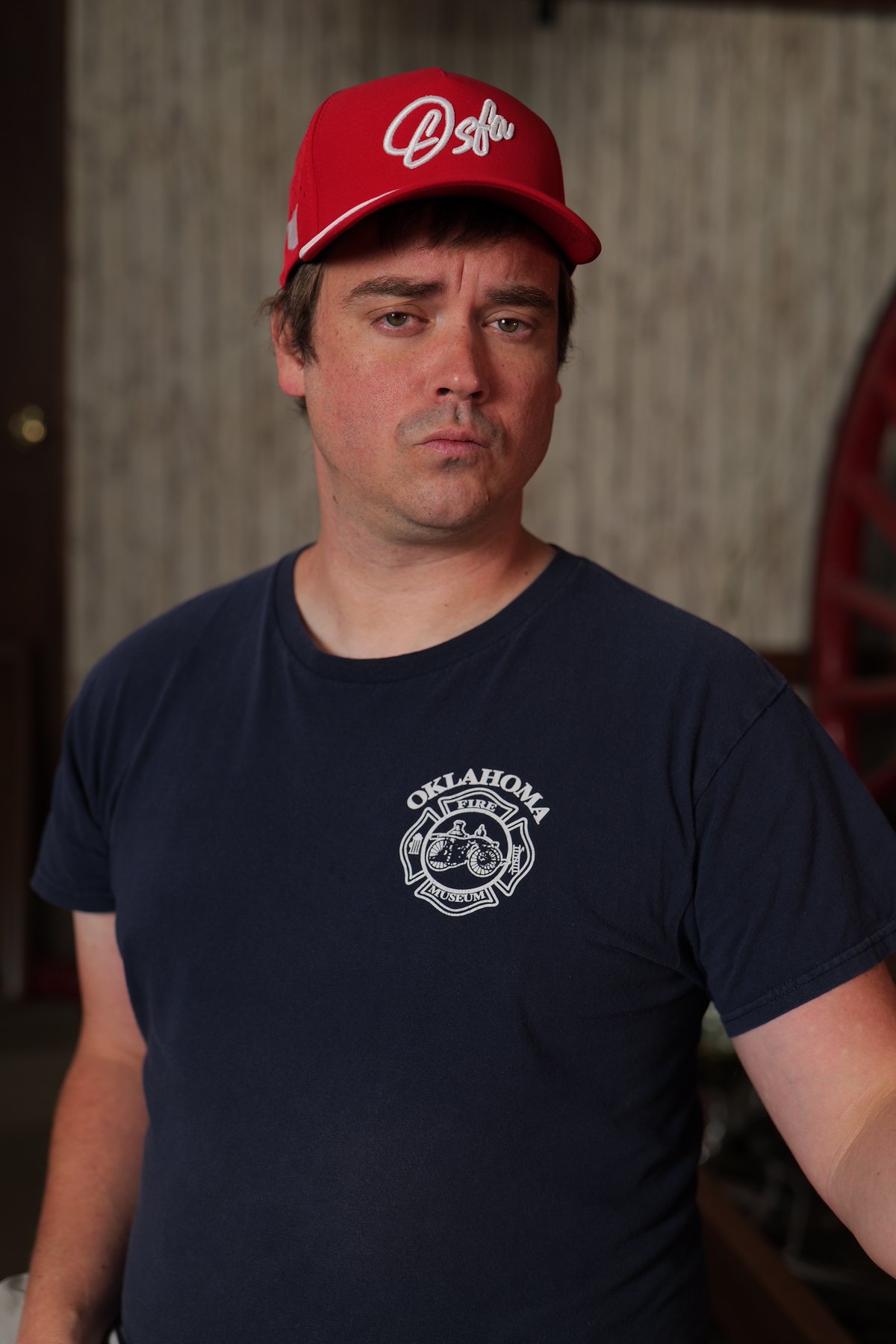 Participant in an Oklahoma Fire Museum shirt wears a red Oklahoma cap during a portrait fundraiser shoot.