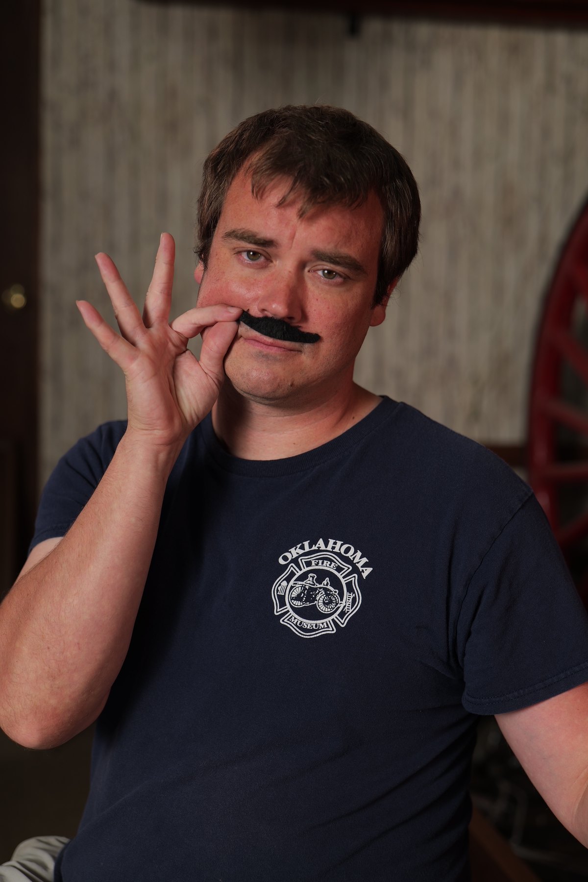 Participant in an Oklahoma Fire Museum shirt poses with a novelty black mustache prop.