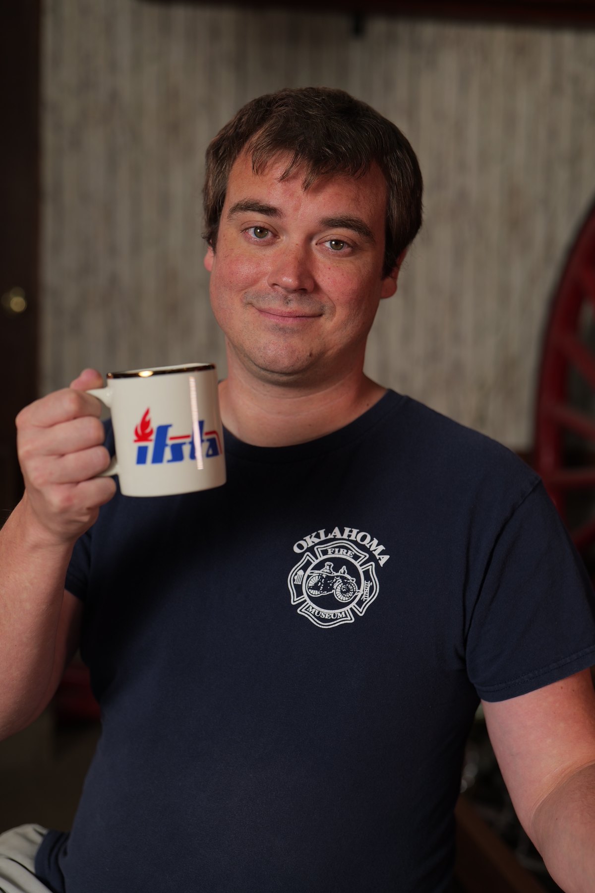 Participant in an Oklahoma Fire Museum shirt holds an IFSTA mug during a portrait fundraiser.