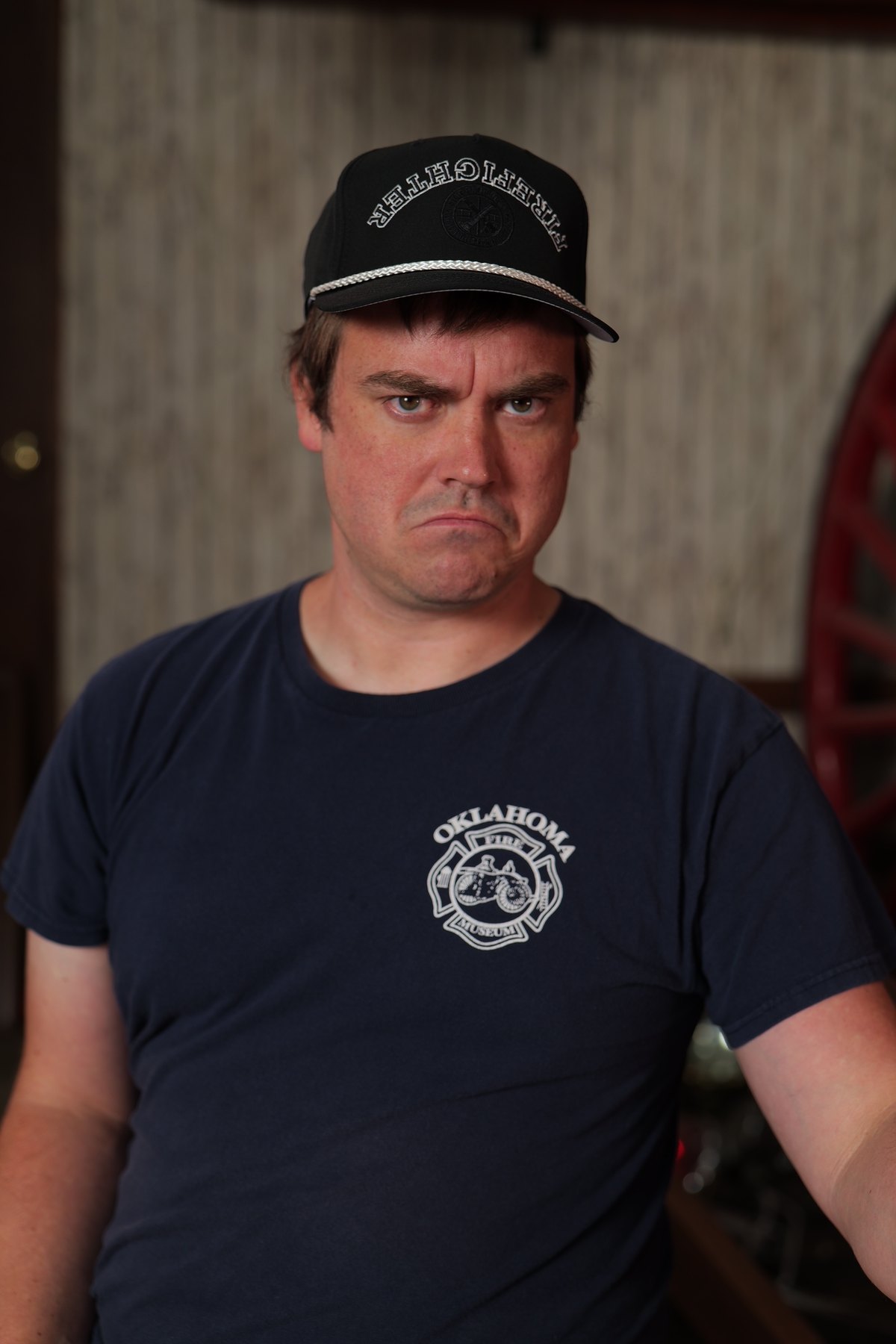 Participant in an Oklahoma Fire Museum shirt wears a black firefighter cap and poses with a stern expression.