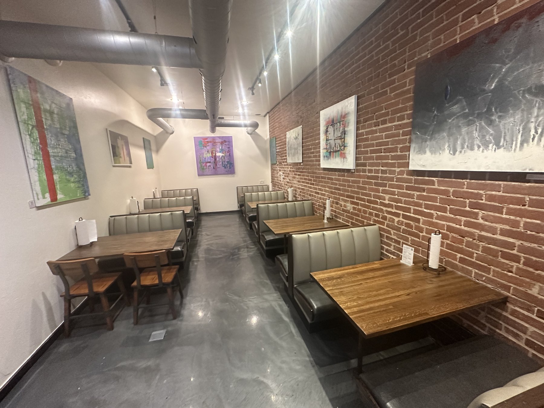 Dining room at BillyGoat Grub in Norman with booth seating, wood tables, exposed brick, and wall art