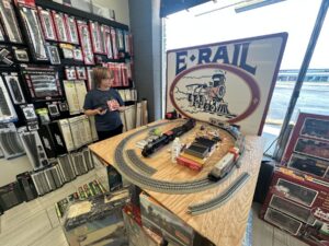 Model train display table inside E-Rail Hobbies in Tulsa with train cars, track pieces, and hobby supplies