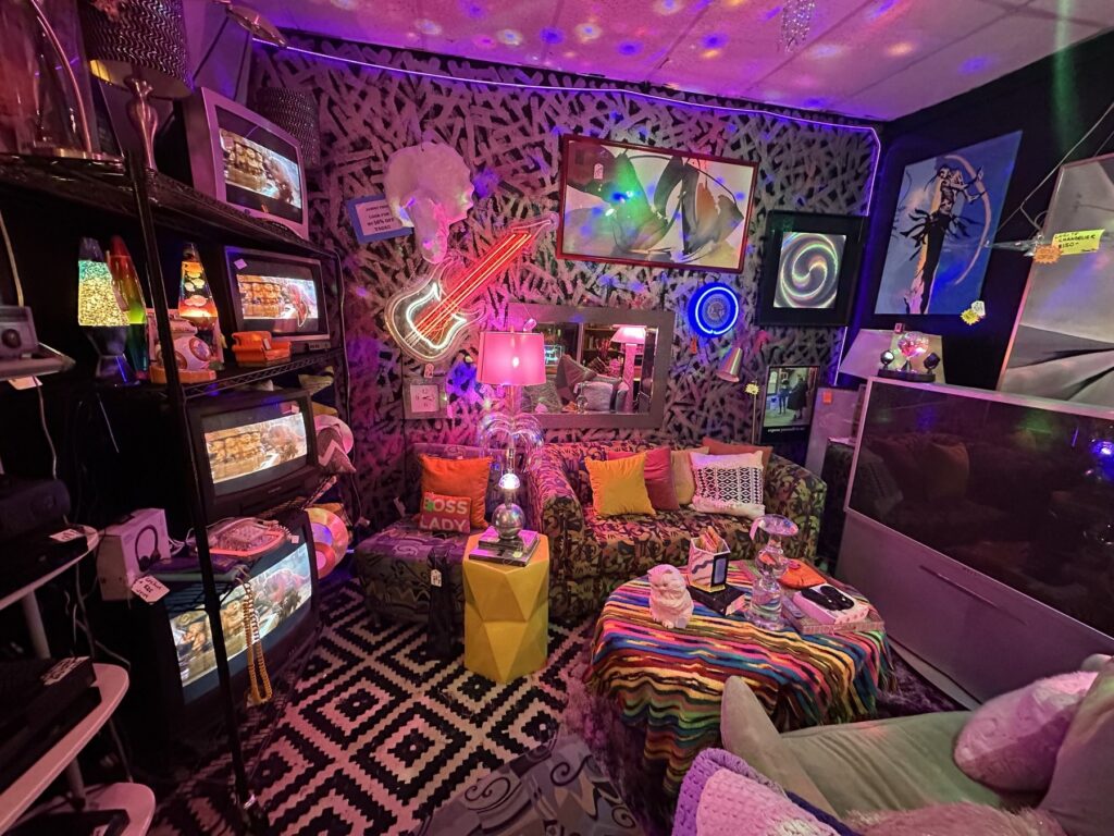 Retro lounge display at Room 3 Vintage with colorful lighting, patterned rugs, framed art, televisions, and vintage furniture.
