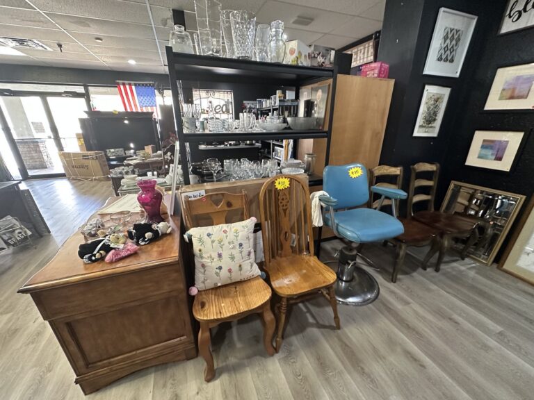 Furniture and decor display at Second Chances Thrift Store with chairs, framed art, glassware, and home items.
