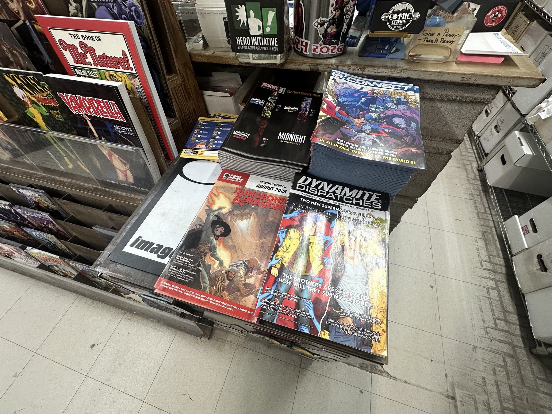 Stacks of new comics and publisher preview books on a display table at The Comic Empire
