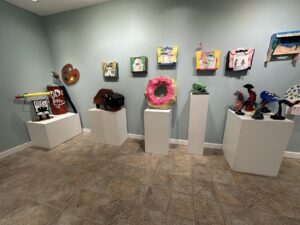 Gallery display at The Firehouse Art Center with student sculptures and colorful artwork on pedestals and walls.