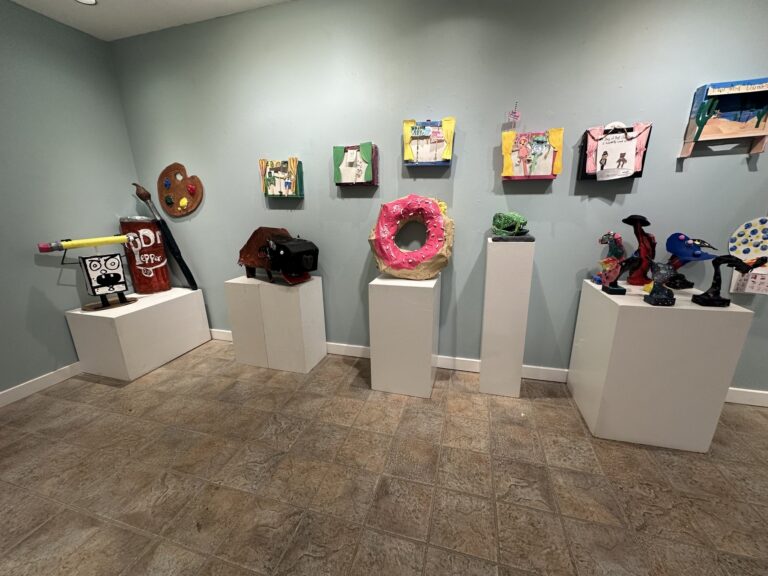 Gallery display at The Firehouse Art Center with student sculptures and colorful artwork on pedestals and walls.
