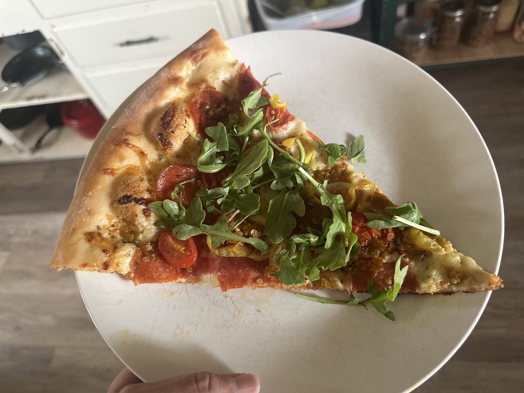 Large Empire Slice pizza slice topped with pepperoni, tomatoes, peppers, melted cheese, and arugula on a white plate.