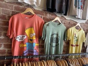 Vintage graphic T-shirts at Wishbone Vintage Clothing including Bart Simpson, Alcatraz, and Minnie Mouse shirts on a brick wall