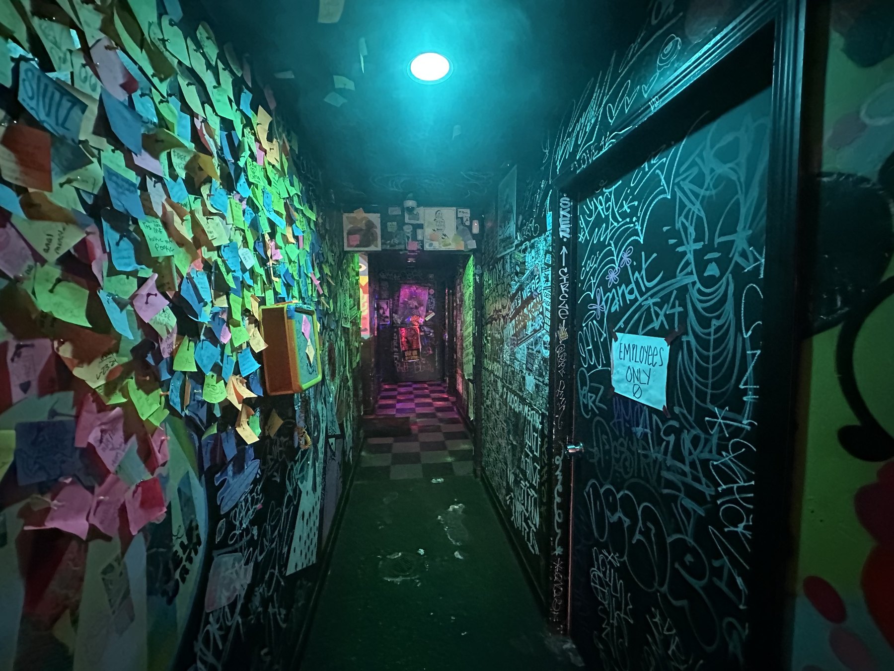 A dark hallway inside Rad Bar covered with graffiti, stickers, and colorful sticky notes.