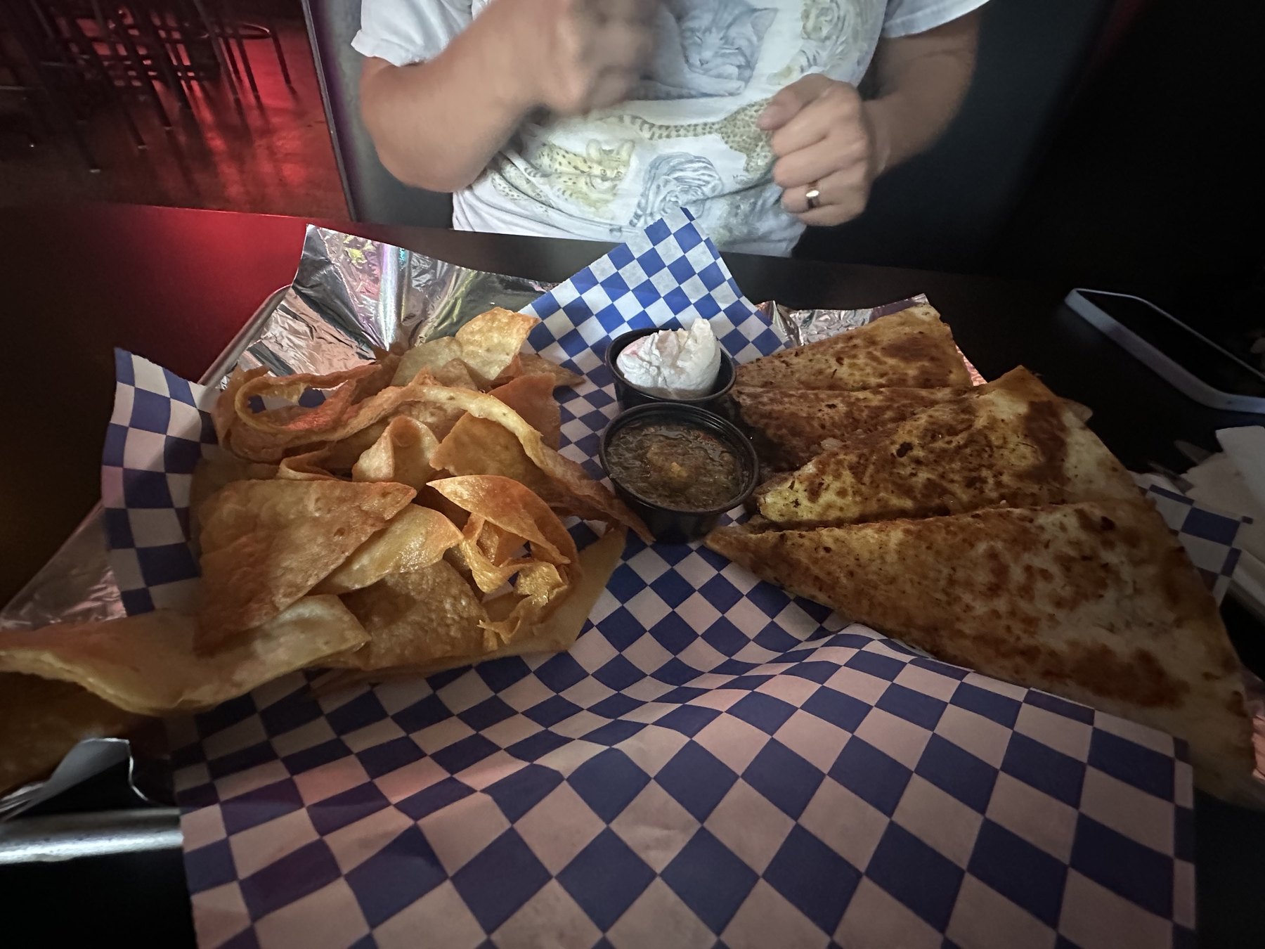A quesadilla at Rad Bar served with tortilla chips and dipping sauces in a blue-checkered paper tray.