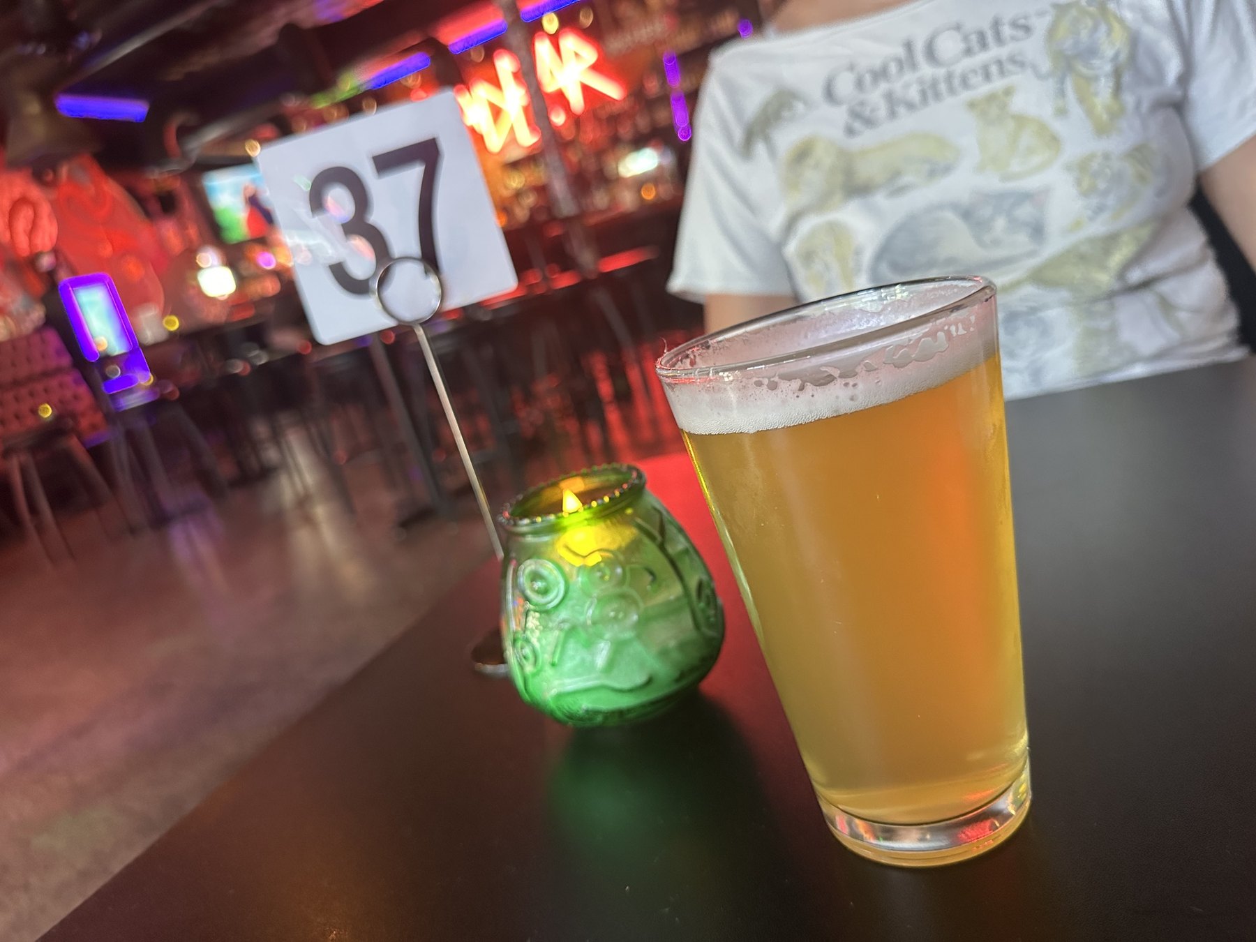 A pint of beer on a table at Rad Bar with a green candle holder and neon bar lights in the background.