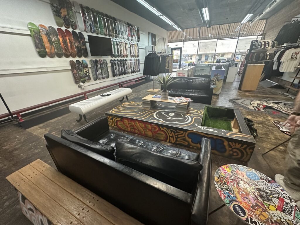 Wide interior view of Money Ruins Everything with couches, a skate obstacle, clothing racks, and skateboard decks on the wall.