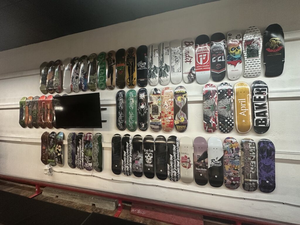 A wall of skateboard decks with varied graphics displayed inside Money Ruins Everything.