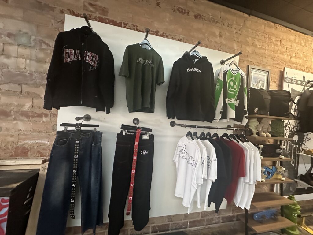 Apparel wall inside Money Ruins Everything with hoodies, shirts, pants, jerseys, and backpacks on display.