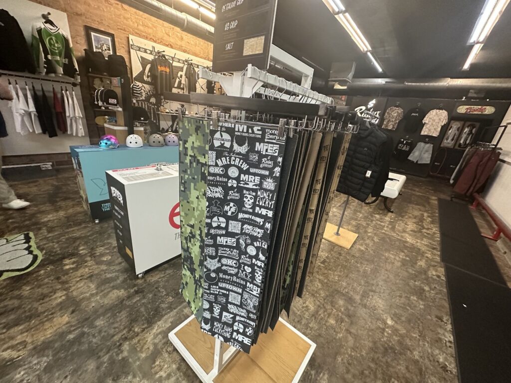 A grip tape display inside Money Ruins Everything with patterned sheets and skate accessories nearby.